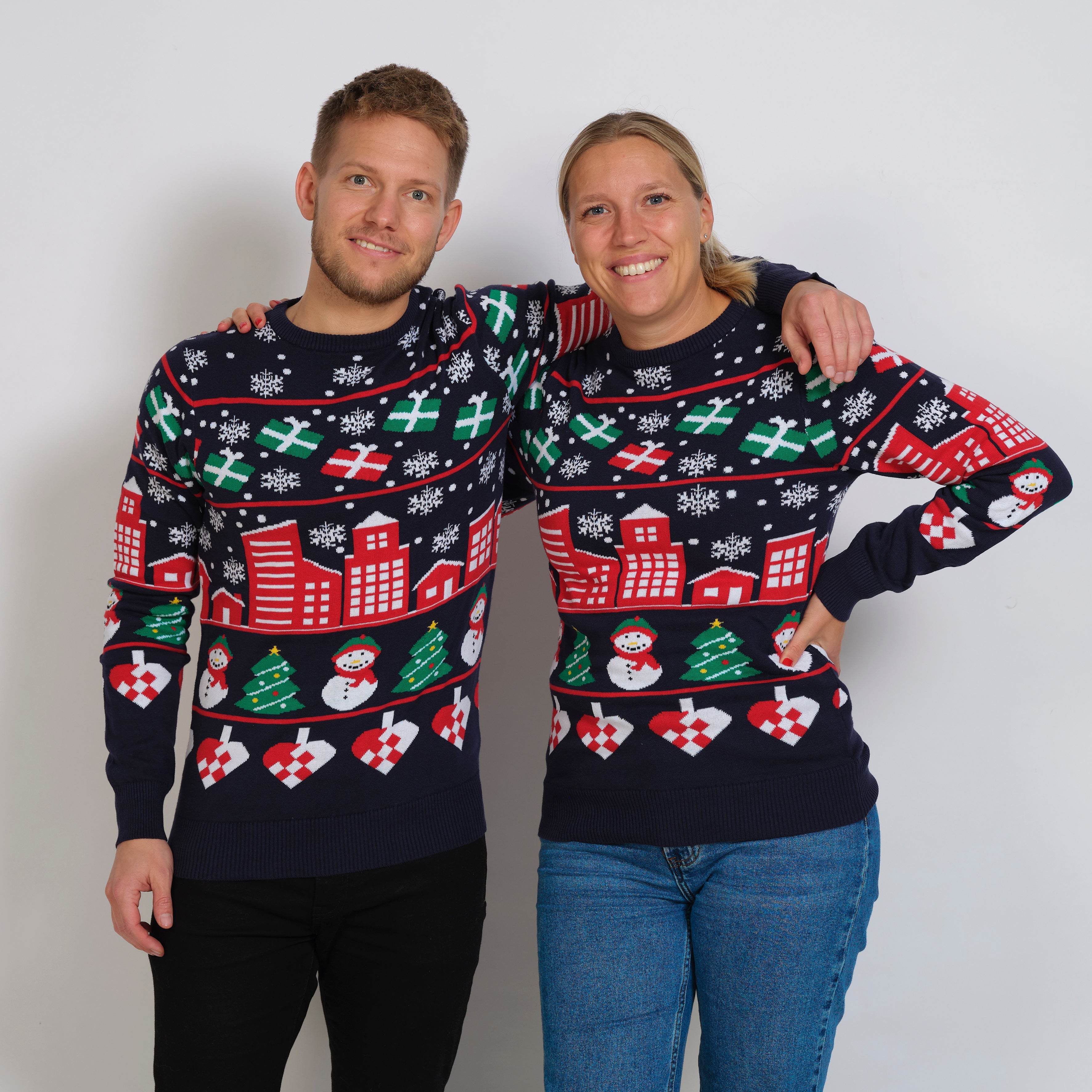 En mand og dame, der holder om hinanden og som begge har en julesweater på, som har et print af en snedækket by.