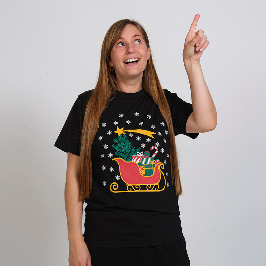 En smilende dame peger op i luften og er iført en sort T-shirt med julemandens slæde på.