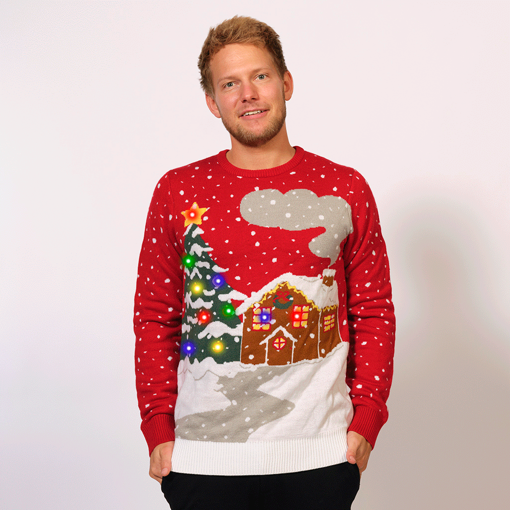 En mand iført en rød julesweater med et blinkende juletræ og et kagehus.