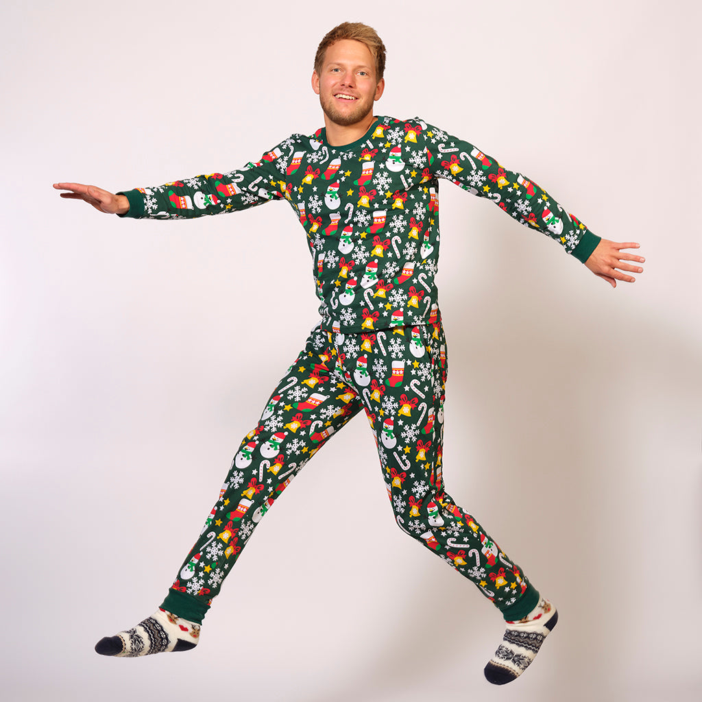 En mand poserer i en grøn julepyjamas med sukkerstokke, snefnug og snemænd på.