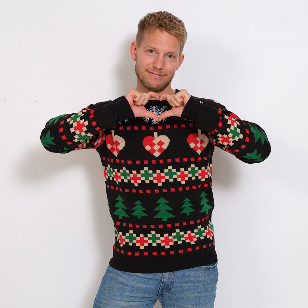 En mand viser et hjertehåndtegn og er iført en sort julesweater med mønster.