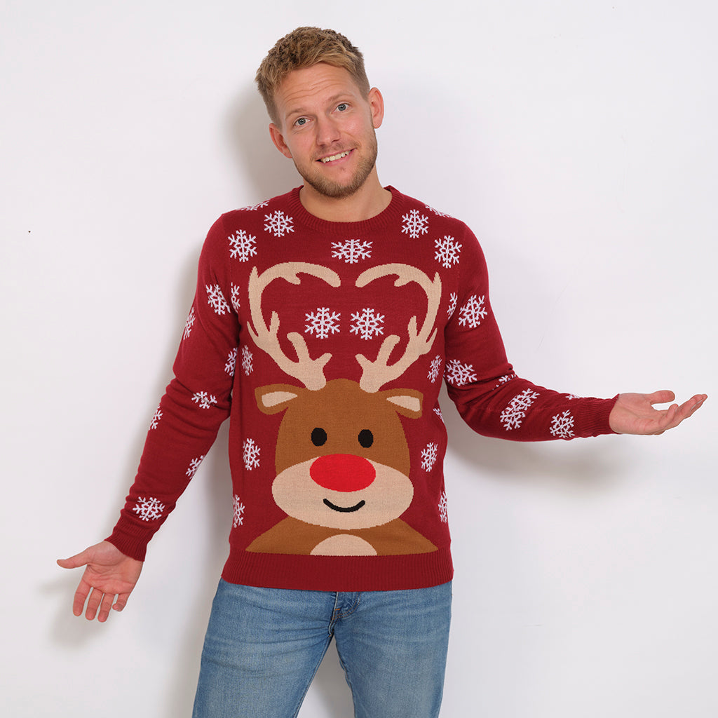 En poserende mand iført en mørkerød julesweater med snefnug og et rensdyr på.
