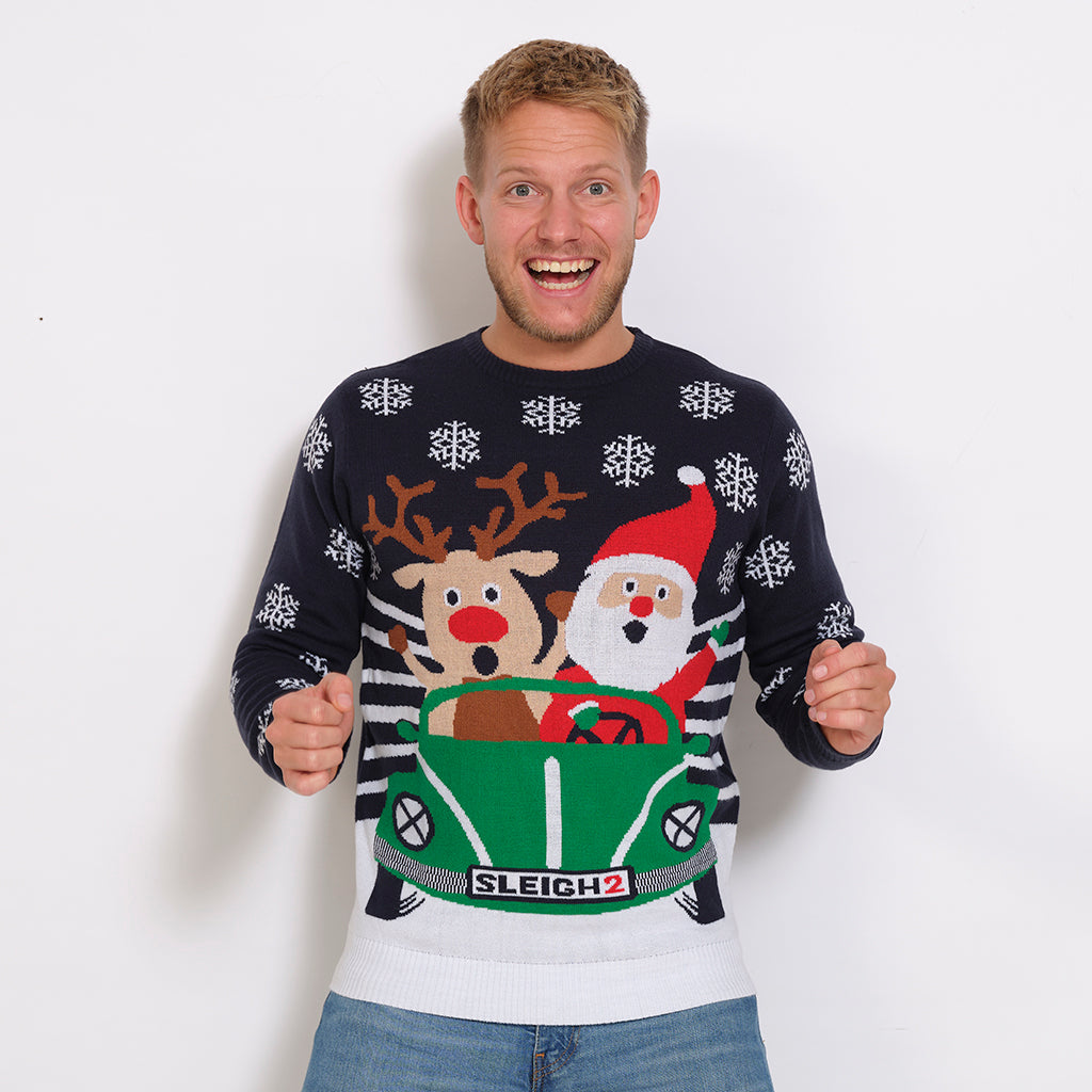 En smilende mand iført en julesweater med en rensdyr og en julemand, der kører bil sammen.