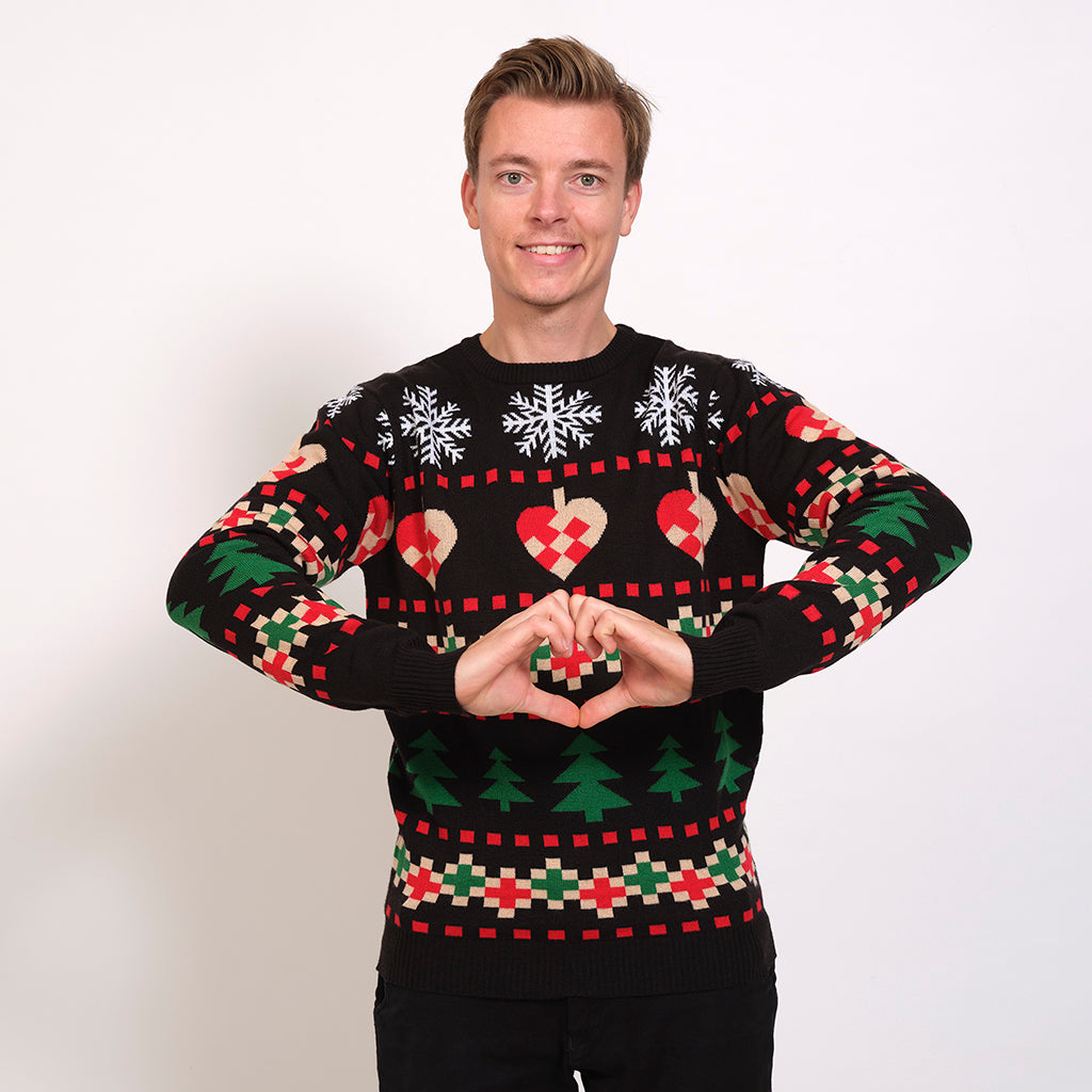 En mand poserer i en sort julesweater med juletræer, julehjerter og snefnug.