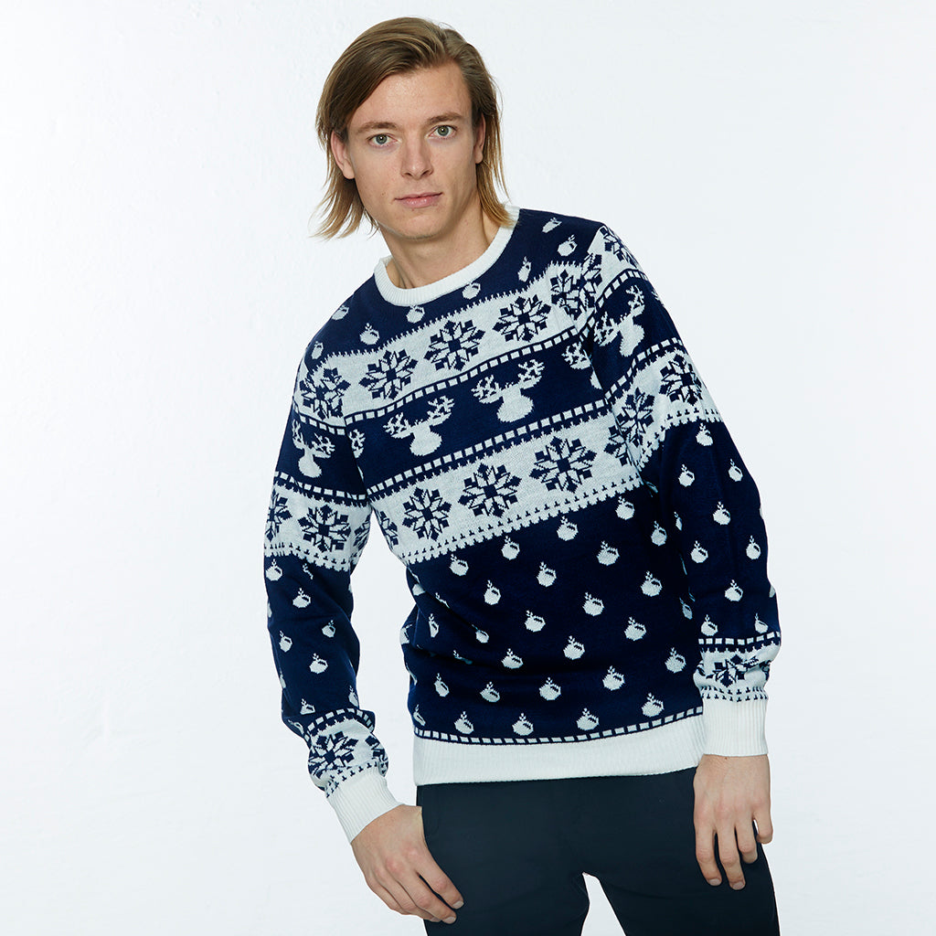 En mand poserer i en dybblå julesweater med rensdyr og snefnug.