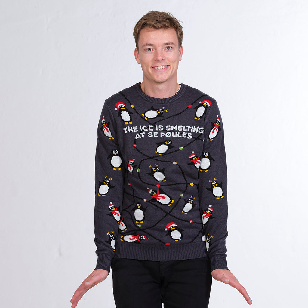 En smilende mand iført en julesweater med pingviner.