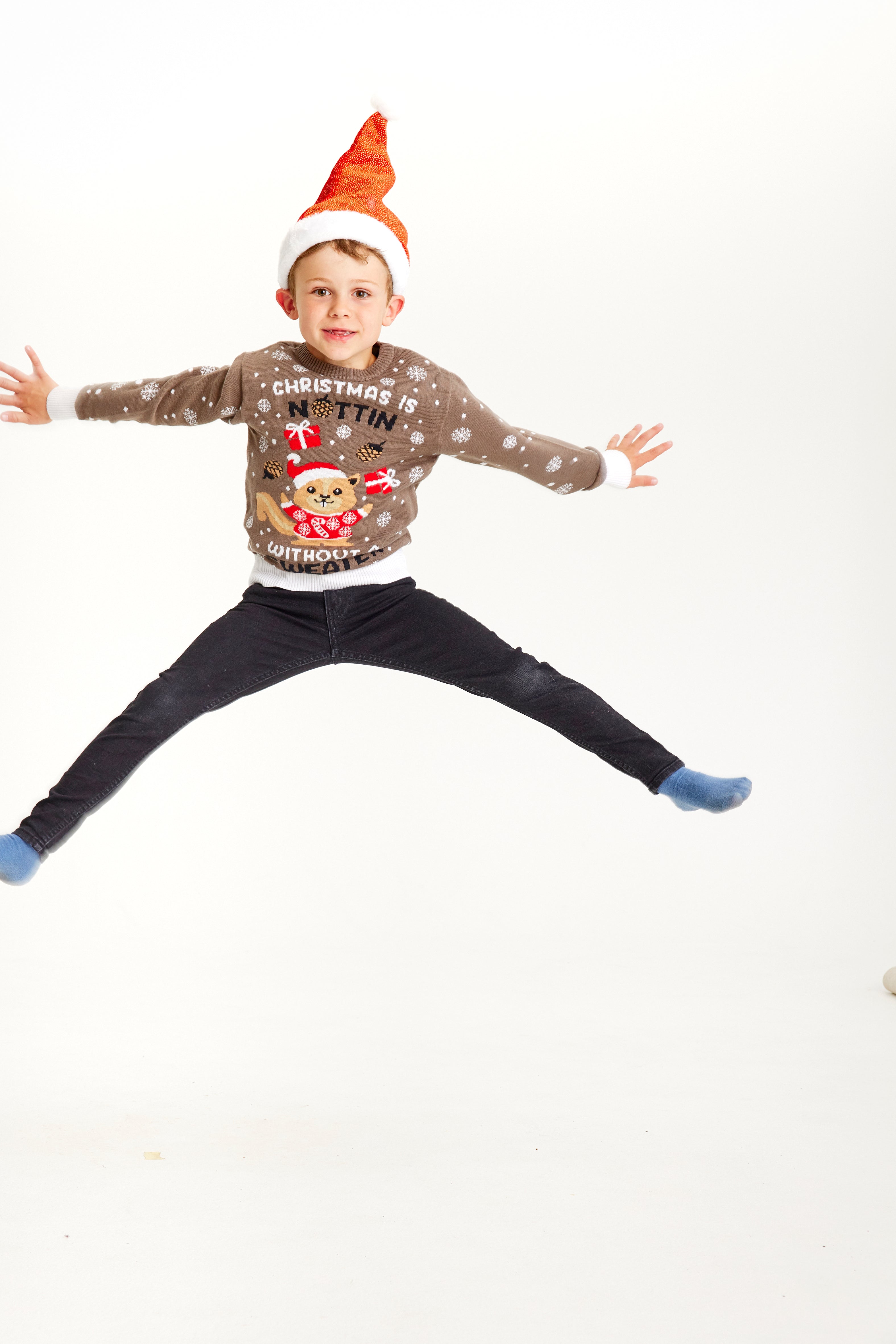 Et hoppende barn iført en julesweater med et egern, der har nissehue på.