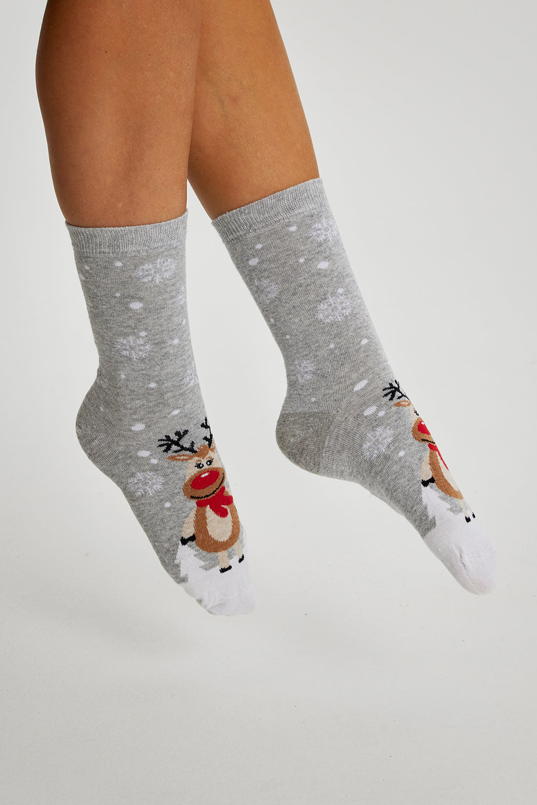 Et par fødder iført grå julesokker med snefnug og rensdyr i et snelandskab.