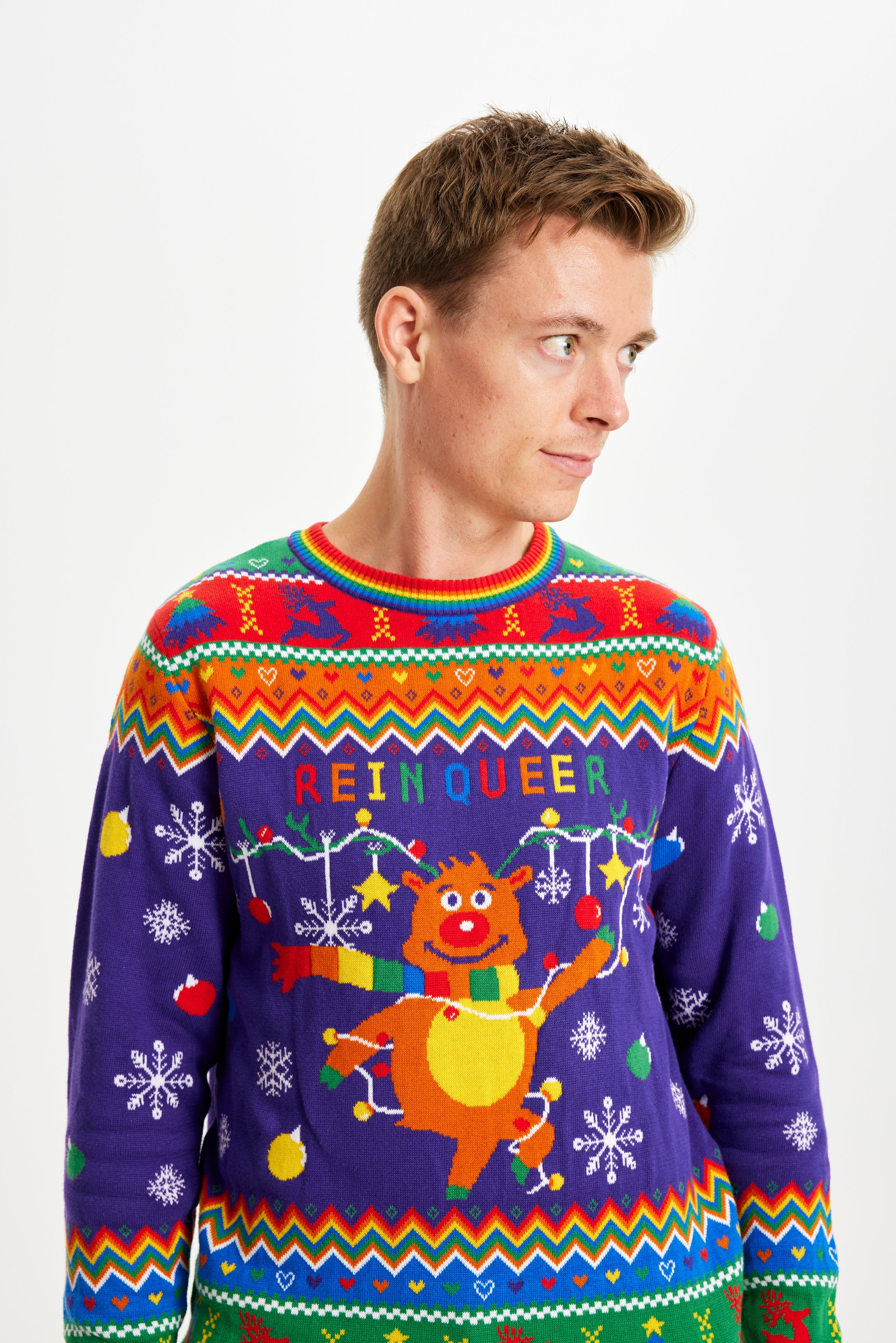 En mand kigger til siden mens han er iført en julesweater med alle regnbuens farver.