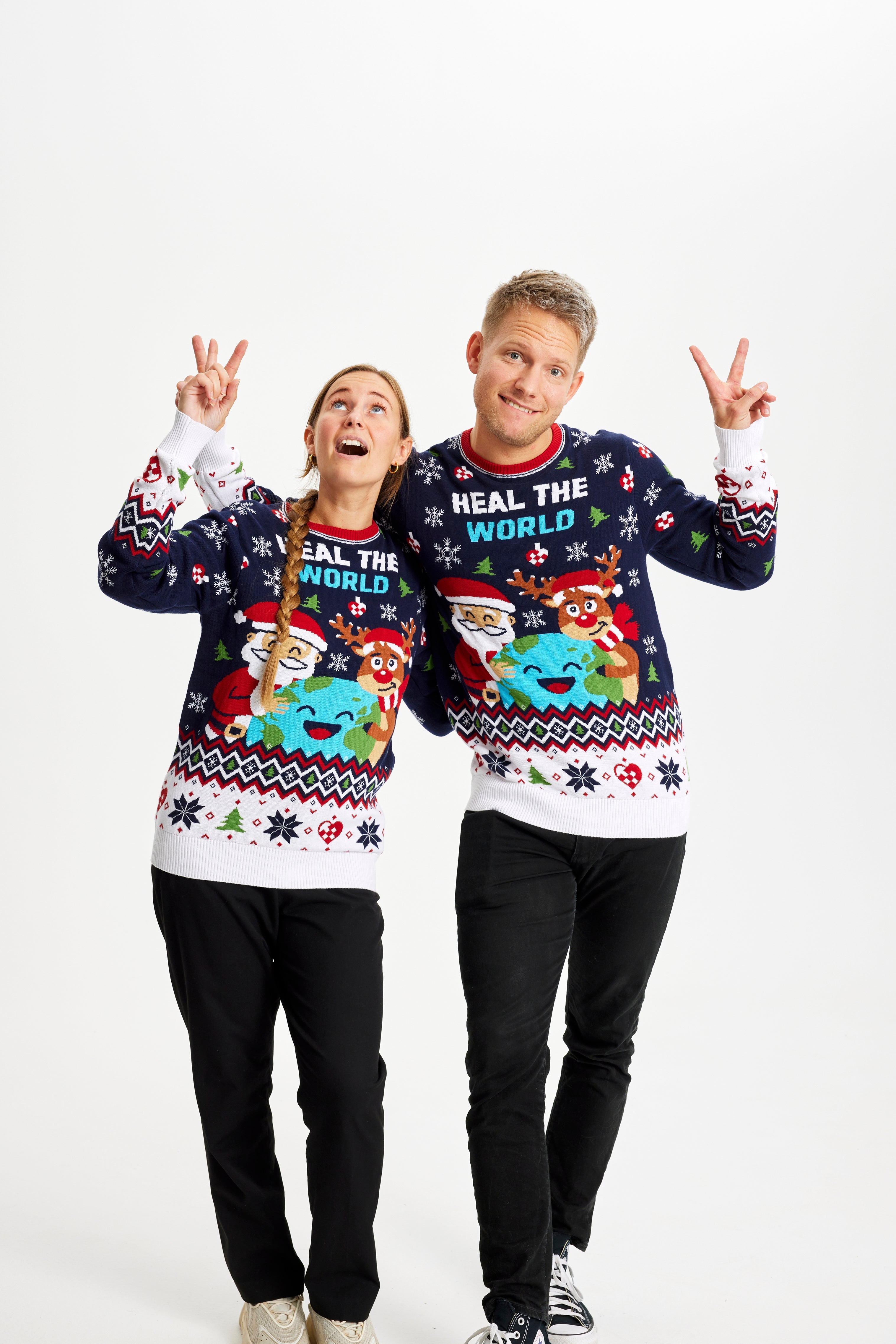 En dame og en mand er begge iført en julesweater og viser peacetegn.
