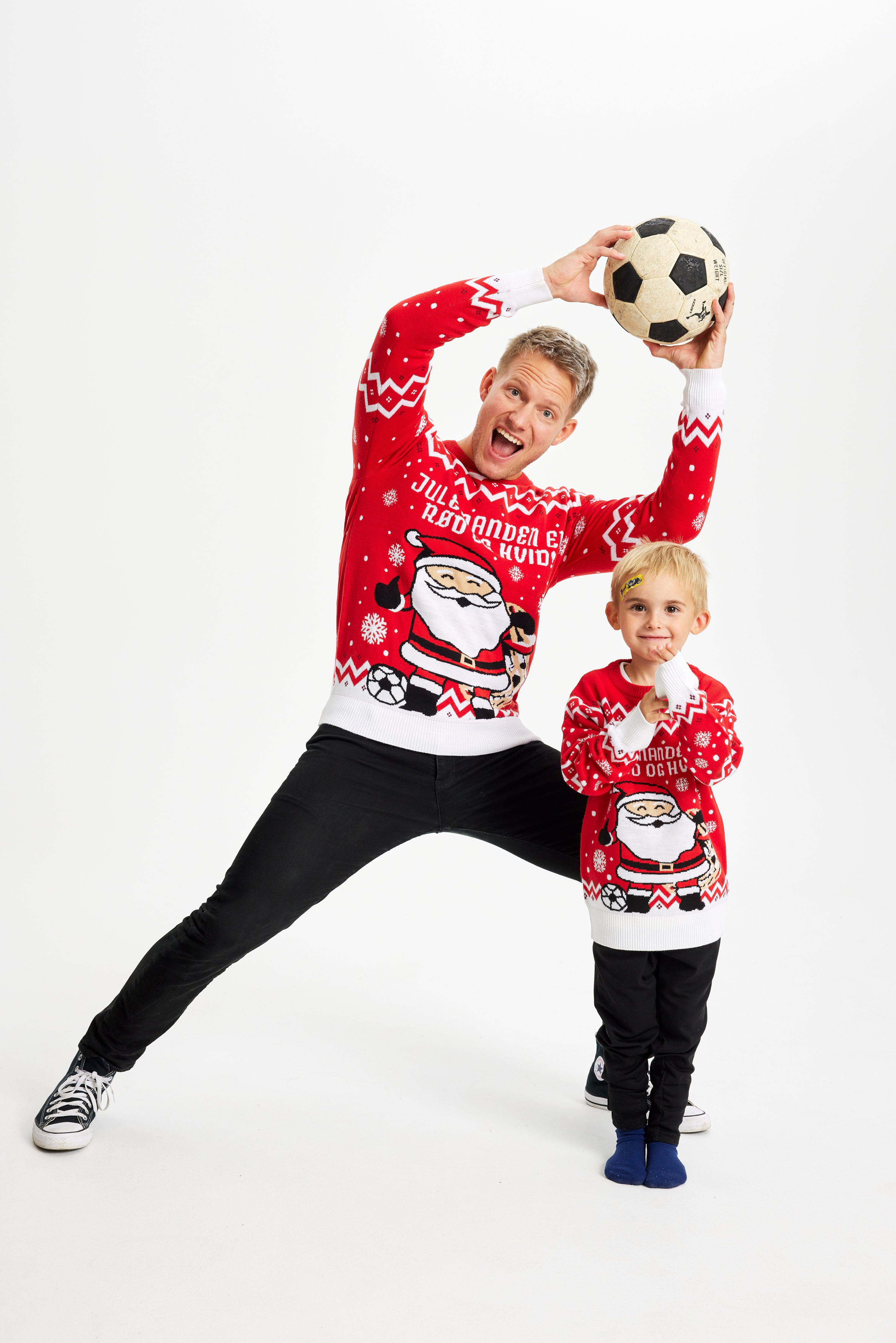 En mand og et barn står med en fodbold og er begge iført en rød julesweater med fodboldtema.