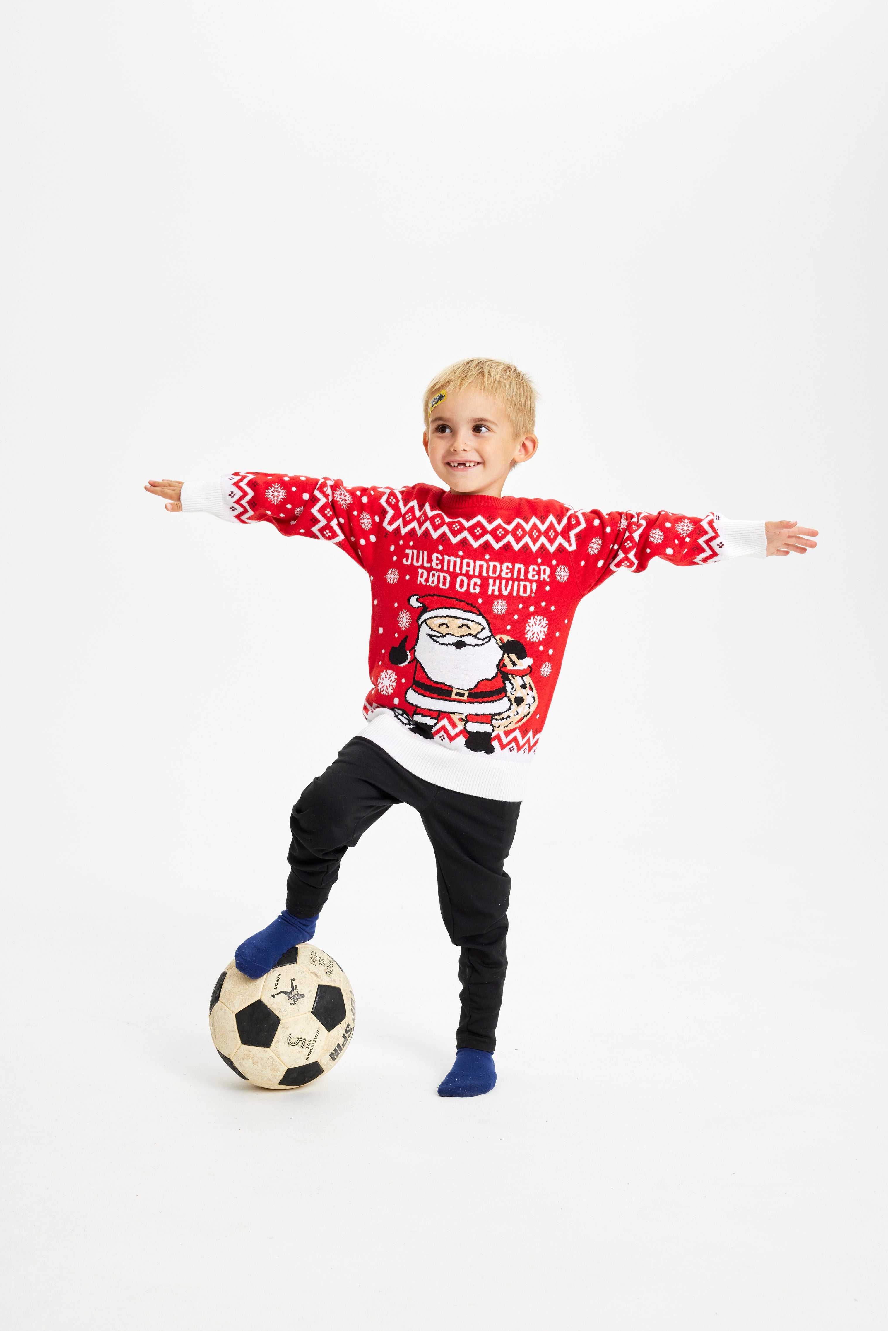 Et barn spiller bold og er iført en rød julesweater.