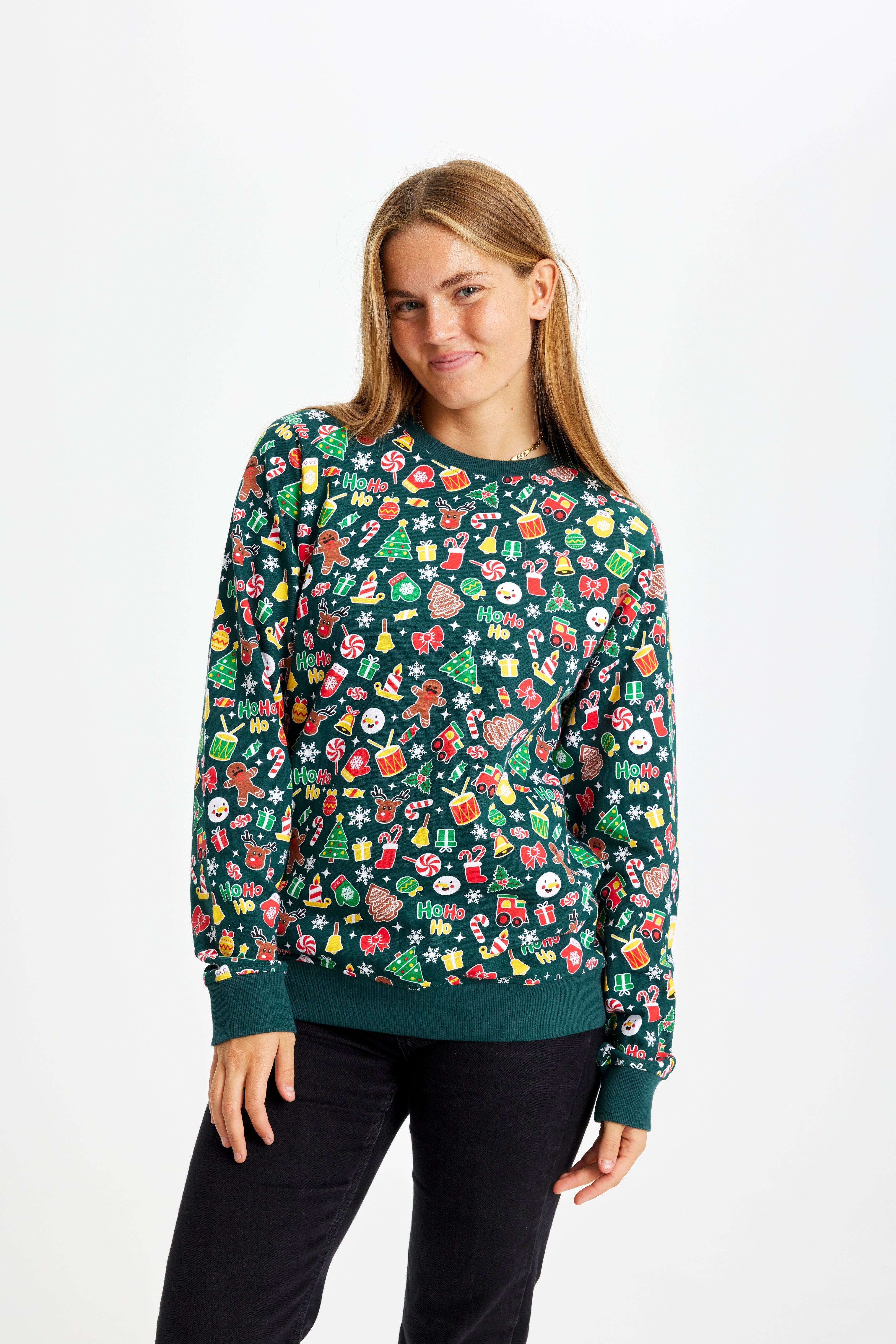 En glad kvinde iført en grøn julesweater med kagemænd, juletræer og trommer på.