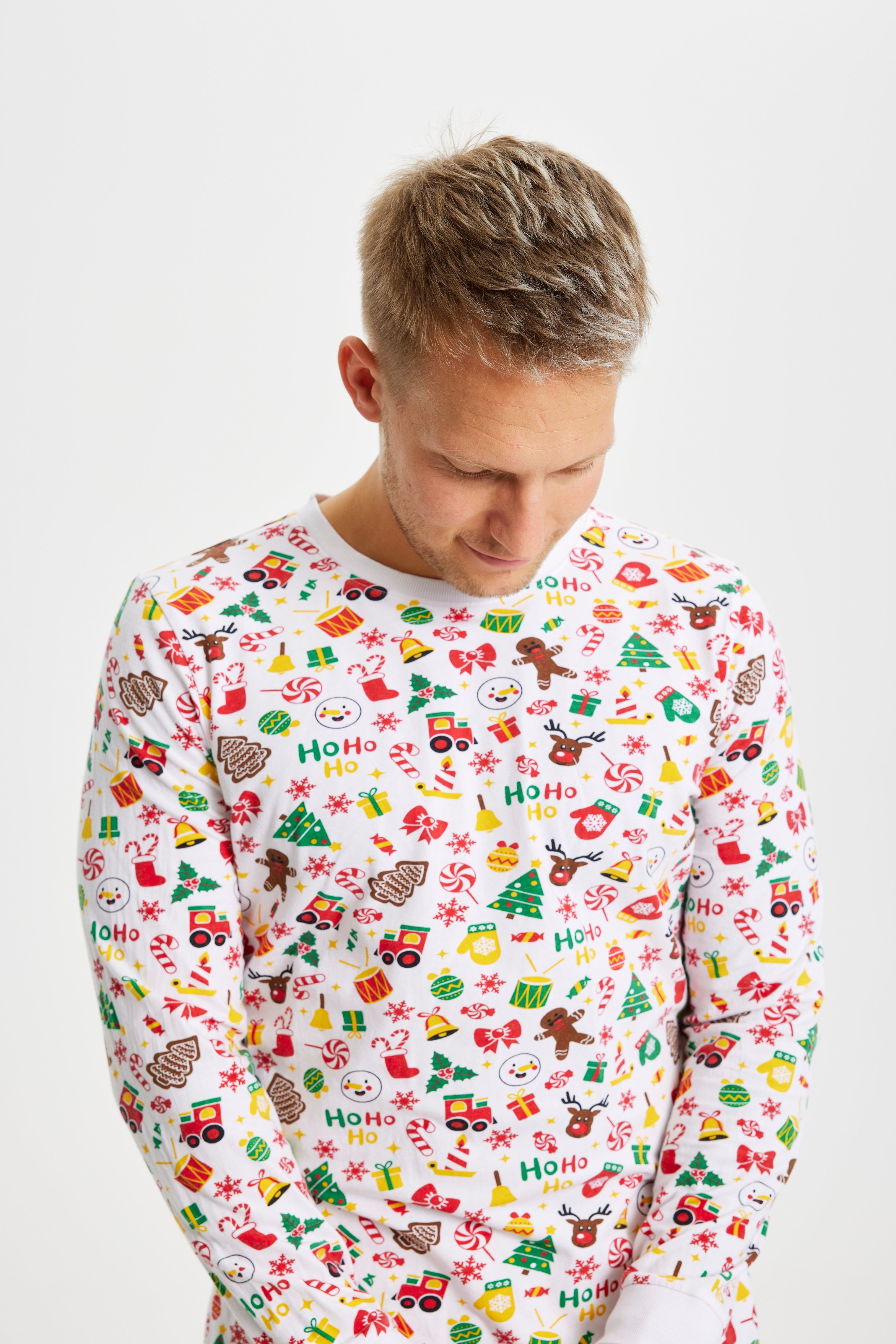 En mand iført en julepyjamas med trommer, juletræer og klokker på.