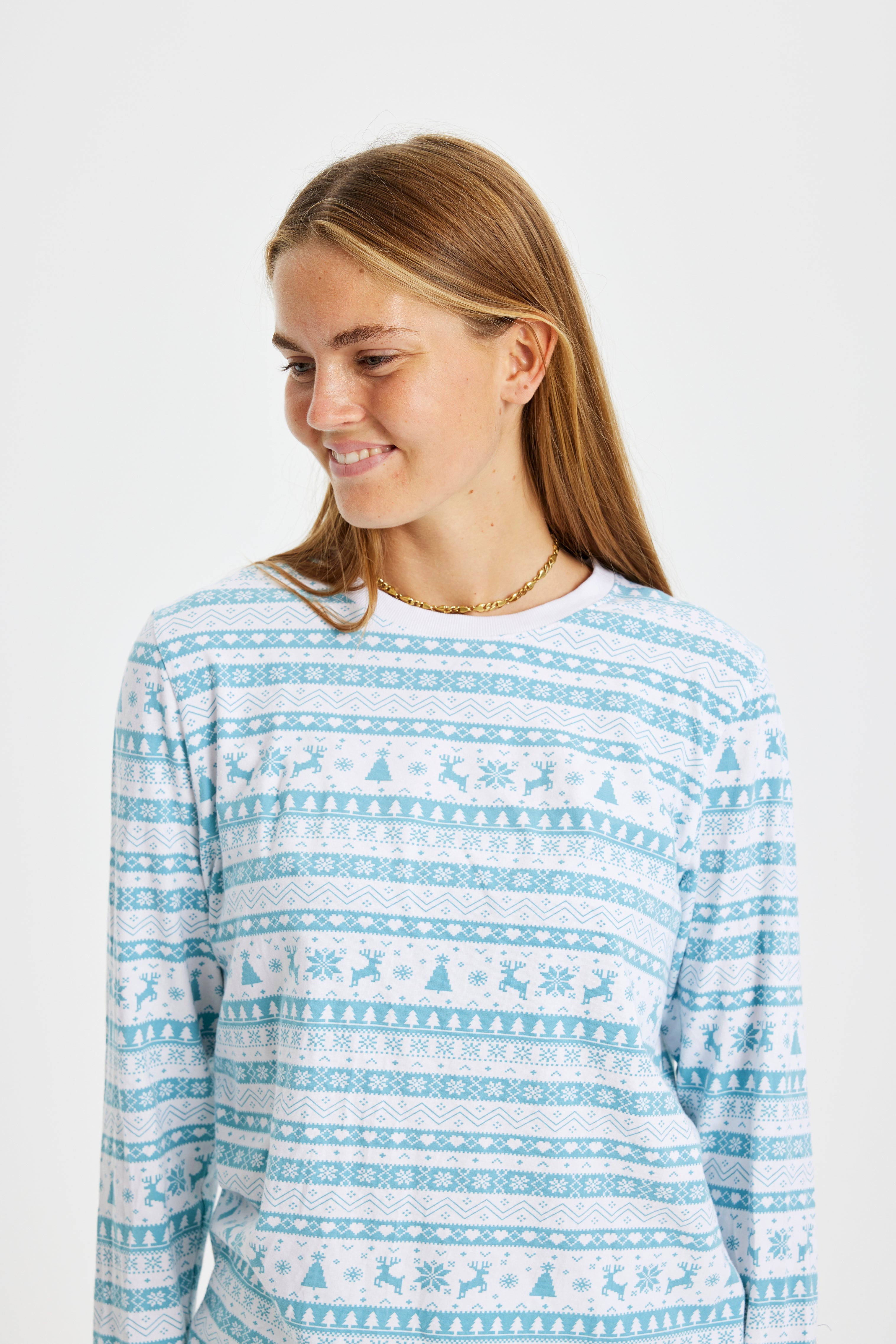 En smilende dame iført en lyseblå og hvid pyjamas med julemønster på.