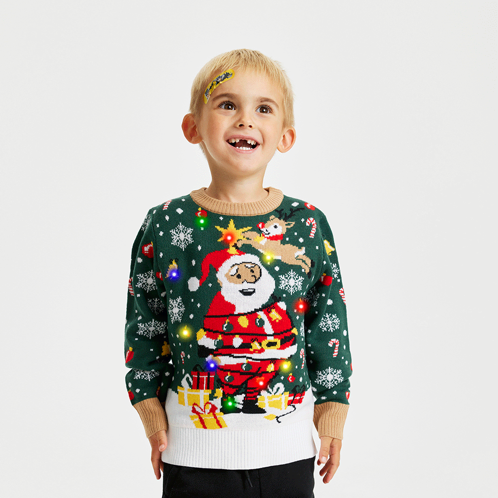 Et smilende barn iført en grøn julesweater med lys på.