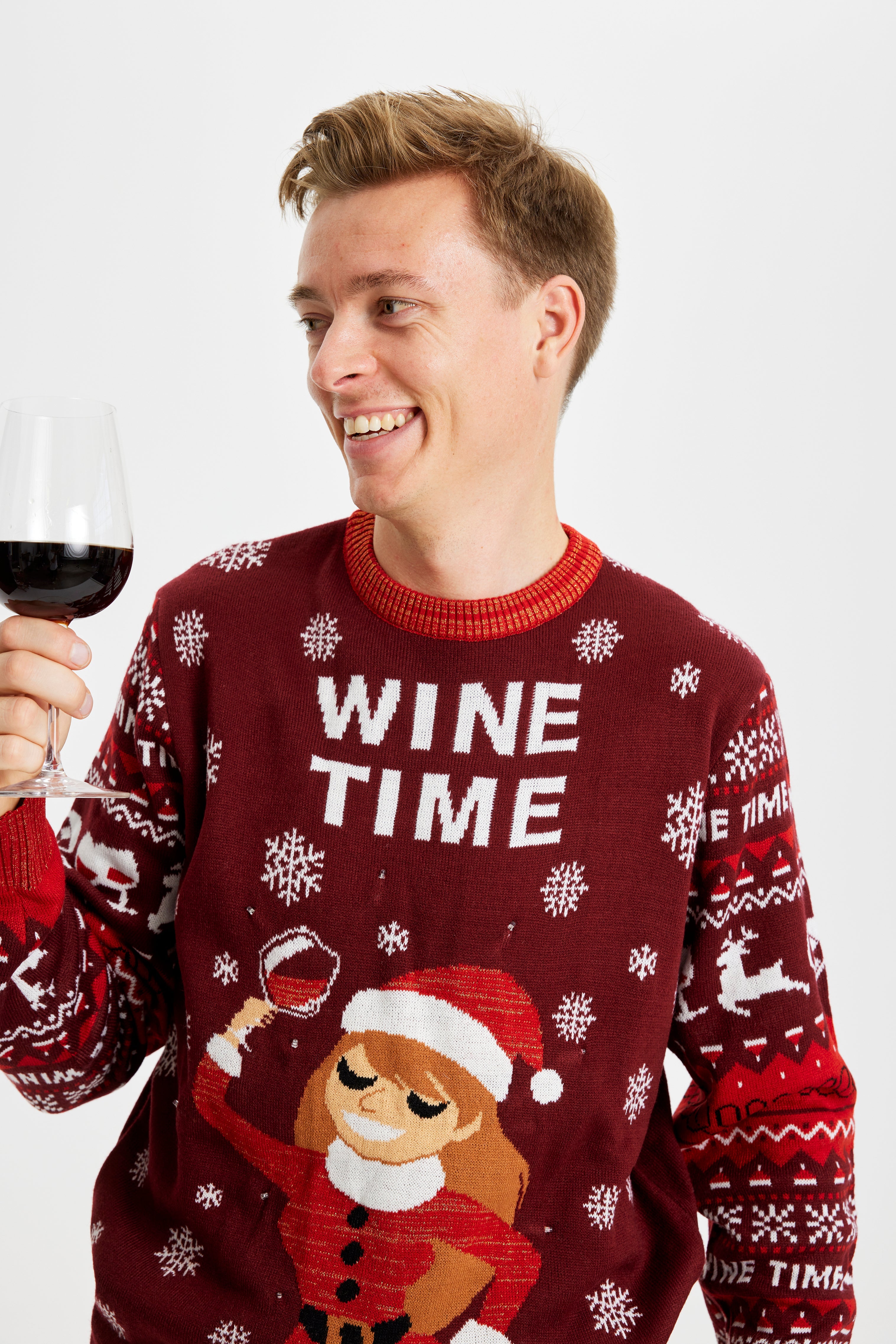 En smilende mand med et glad vin iført en rød julesweater.