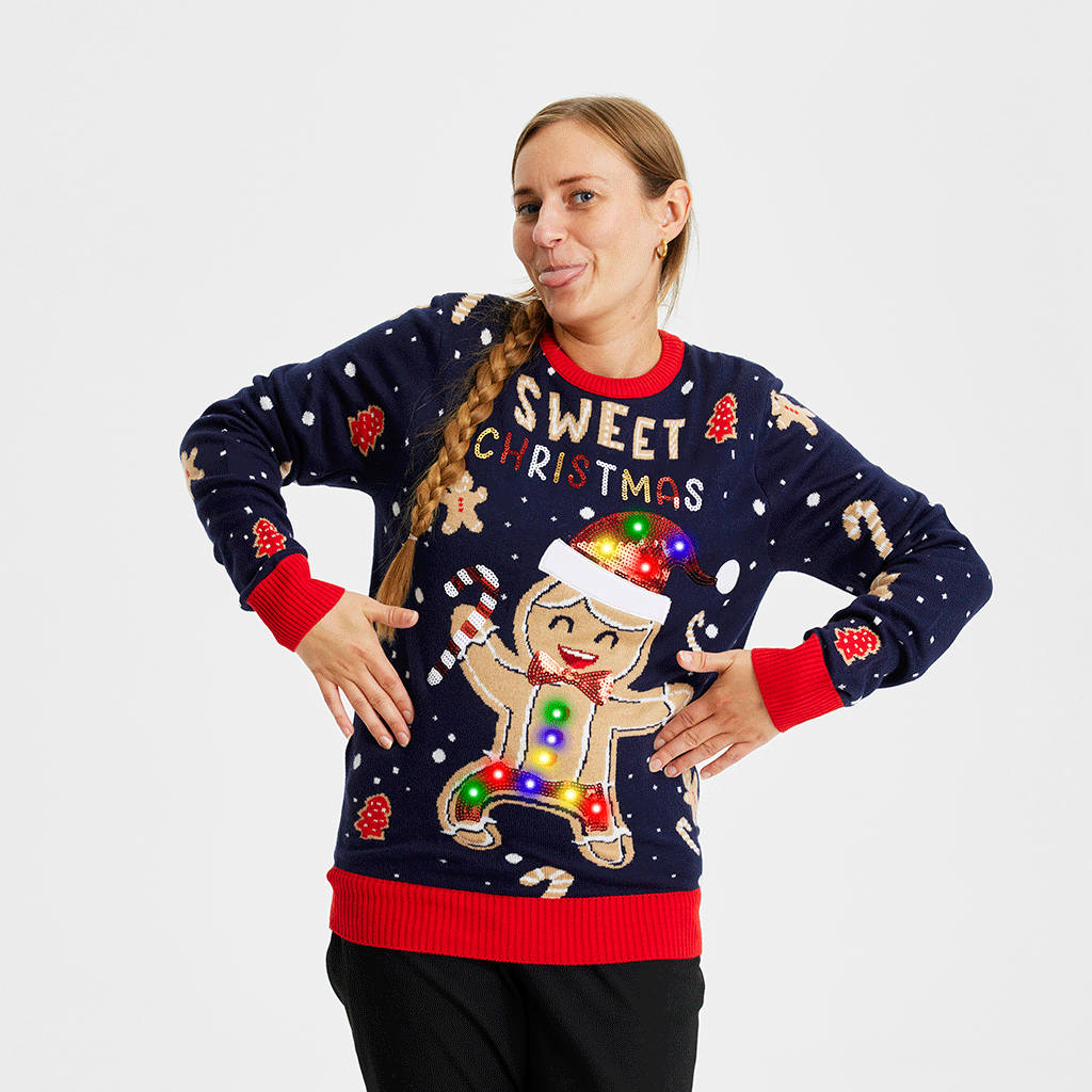 En glad dame iført en dybblå julesweater med en lysende kagemand med nissehue på.