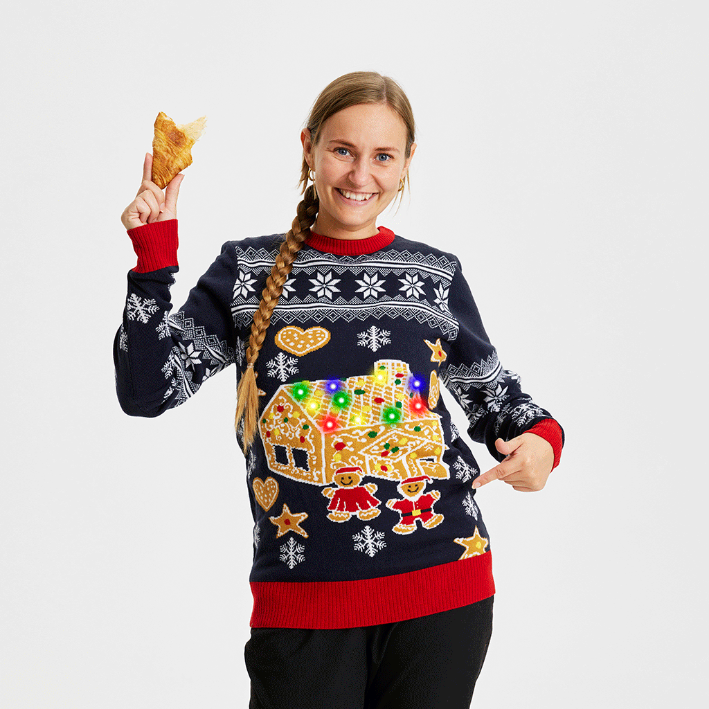 En dame står med en halv croissant i hånden pg er iført en julesweater med lys, der blinker i forskellige farver.