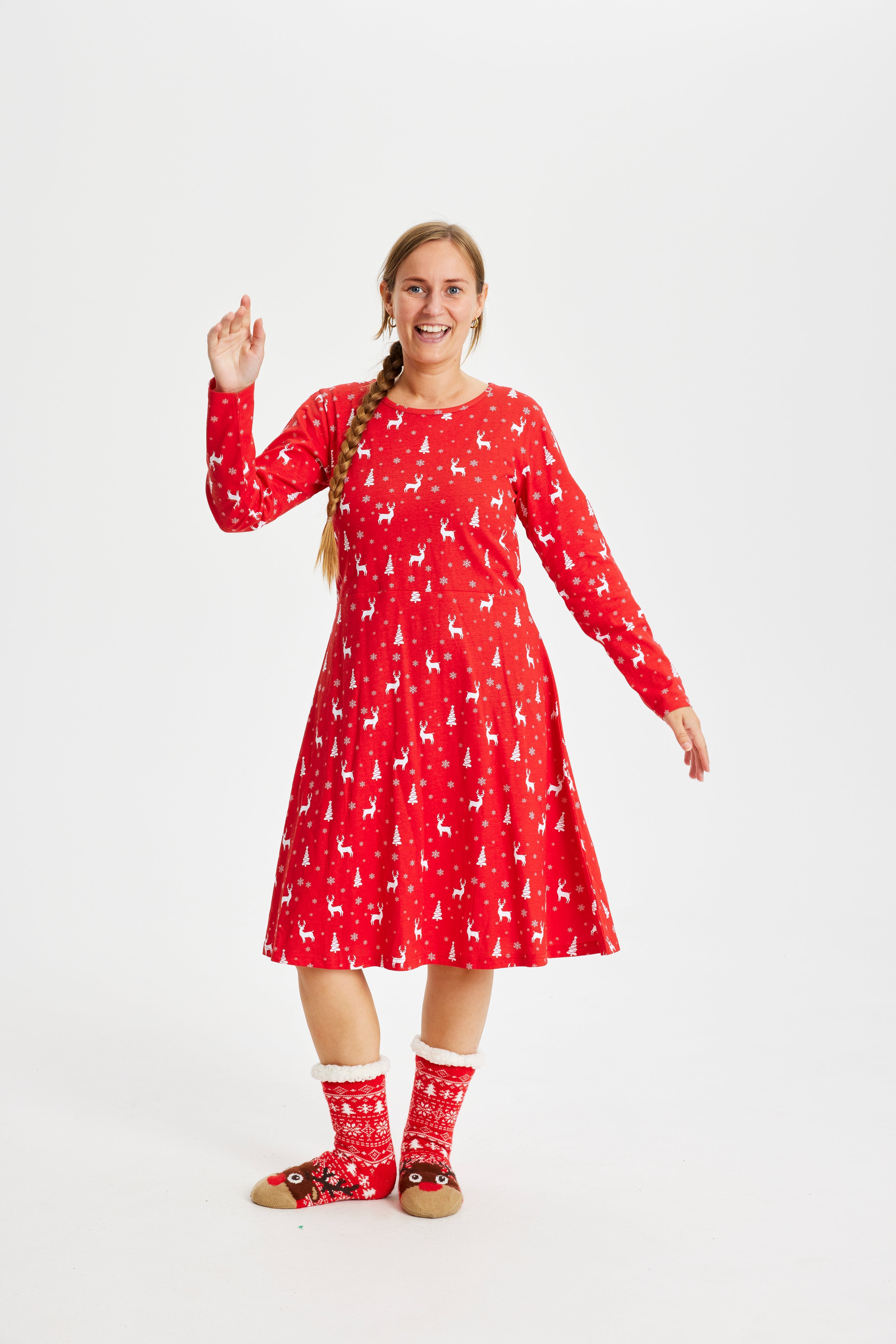 En kvinde iført en rød julekjole holder den ene hånd i vejret, mens hun poserer.