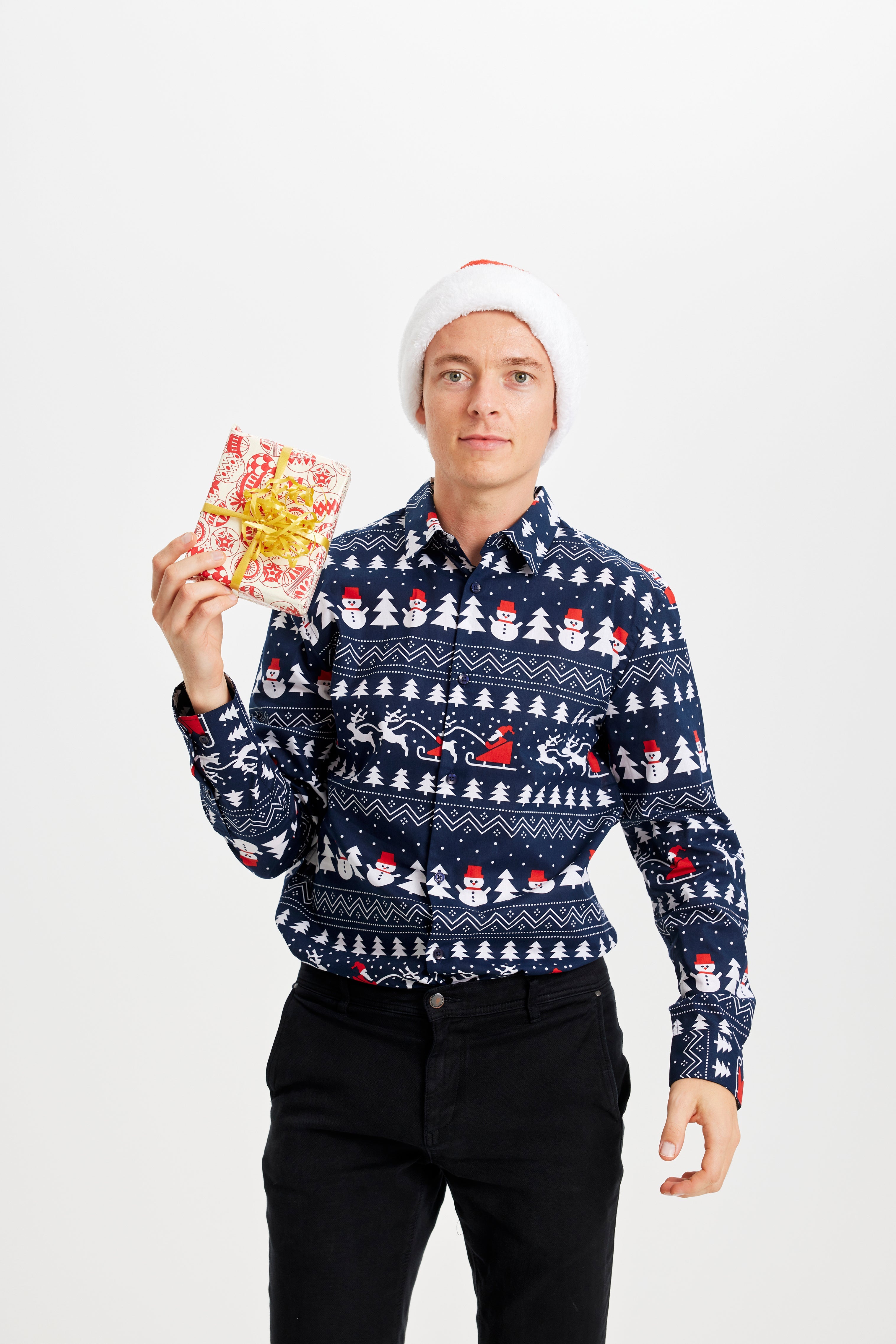 En mand med nissehue og en gave i hånden og er iført en blå juleskjorte.