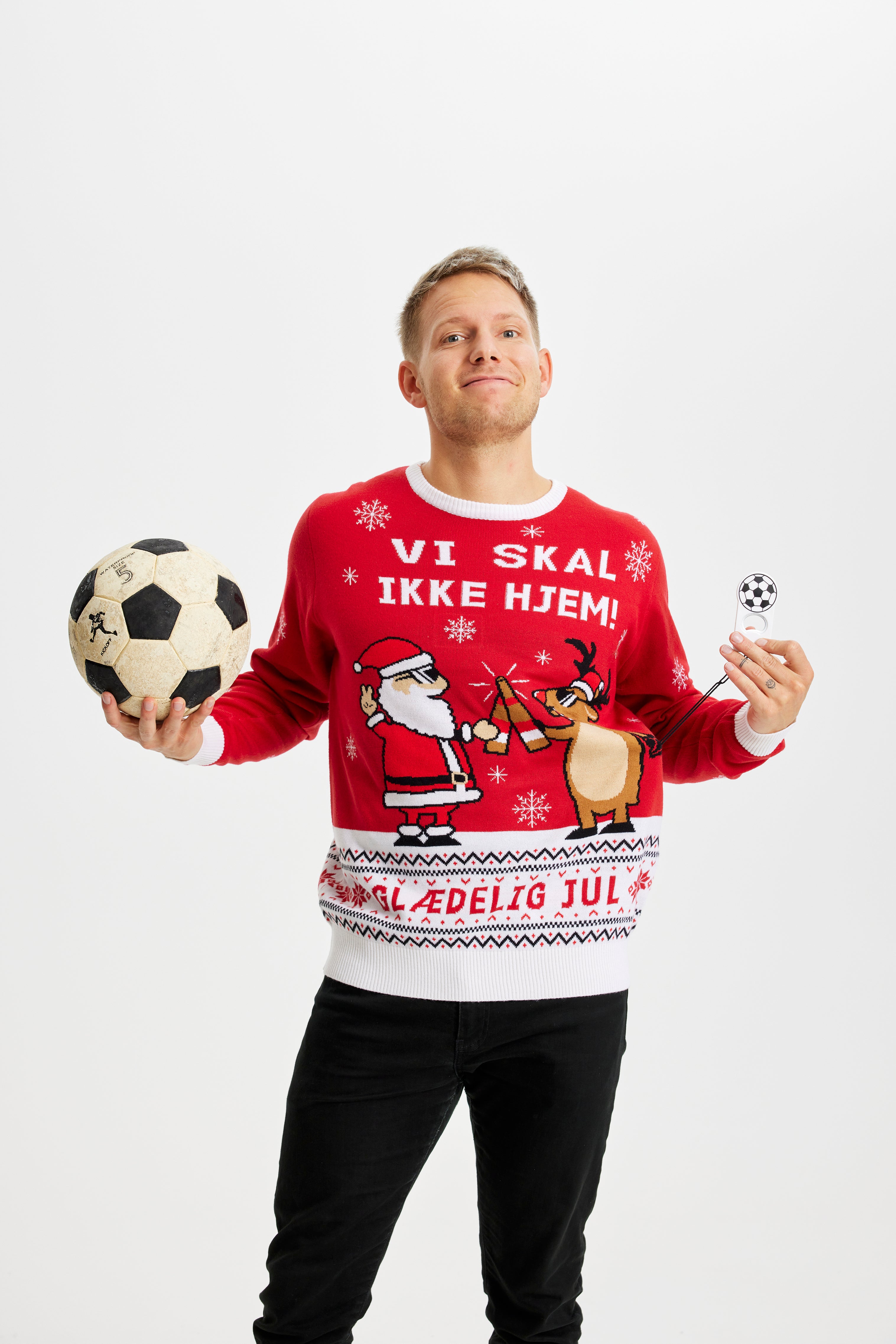 En mand med en fodbold i hånden iført en julesweater i rød.