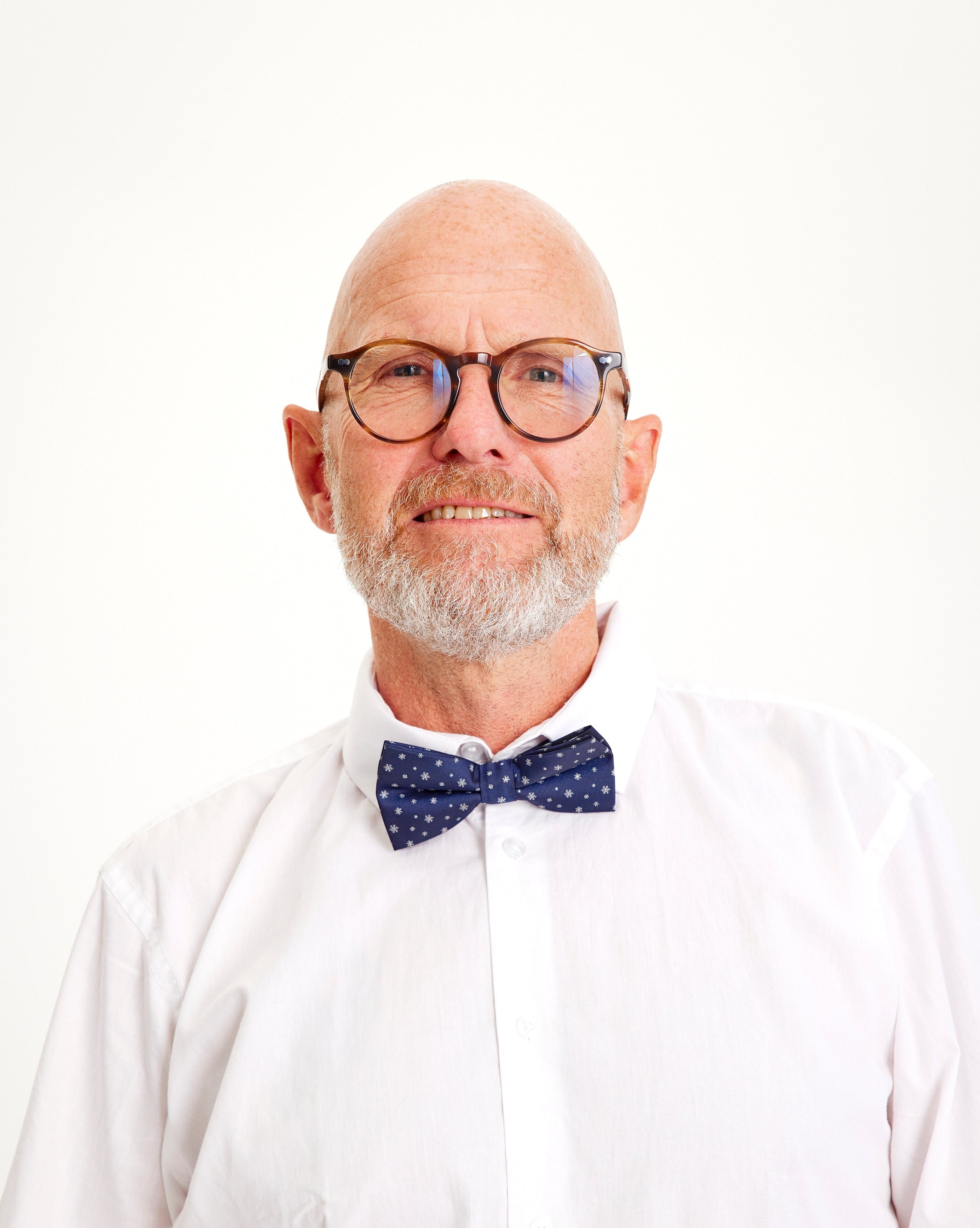 En mand med briller iført en hvid skjorte og en blå butterfly med stjerner på.