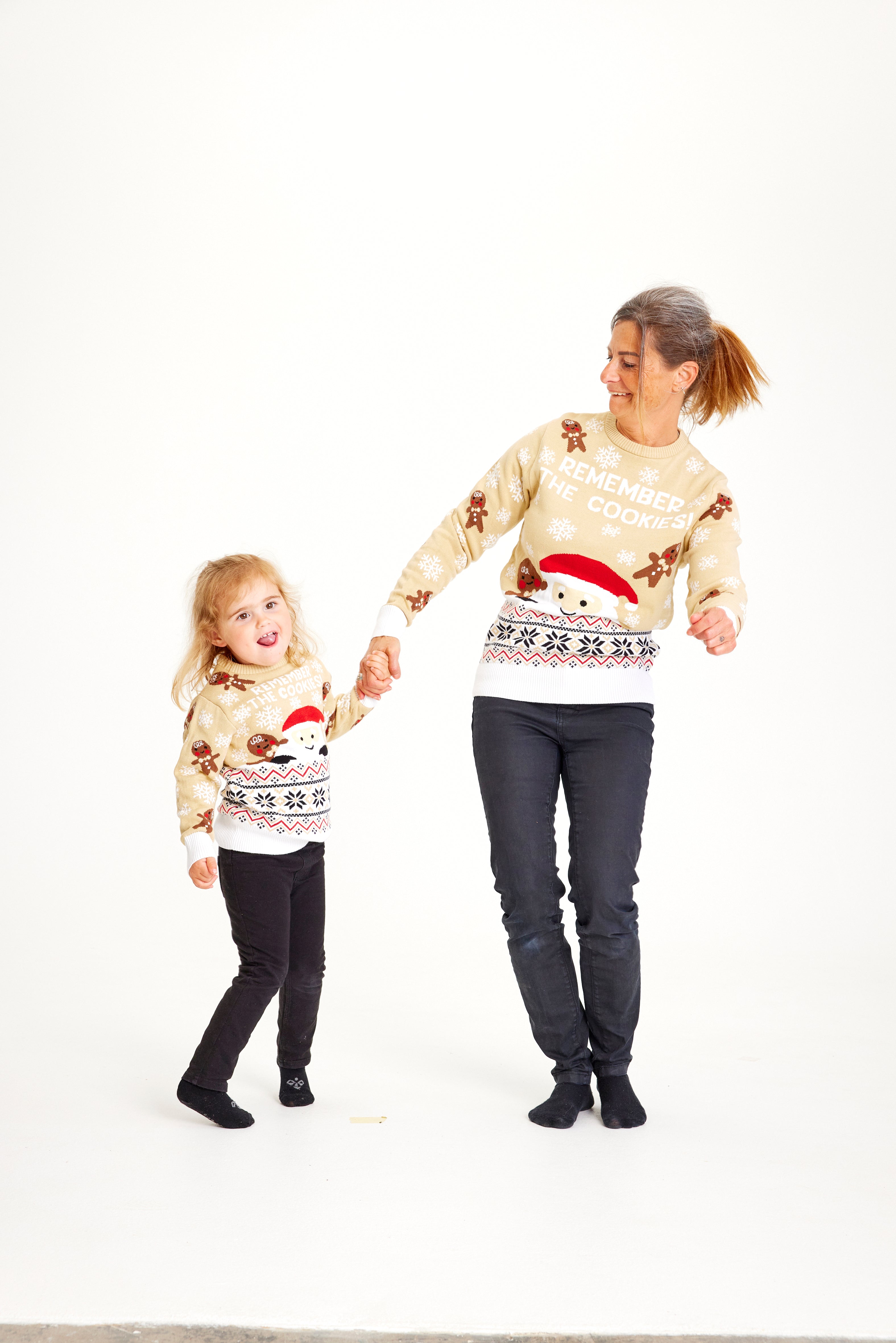En dame og et barn holder i hånd og er iført en beige julesweater.