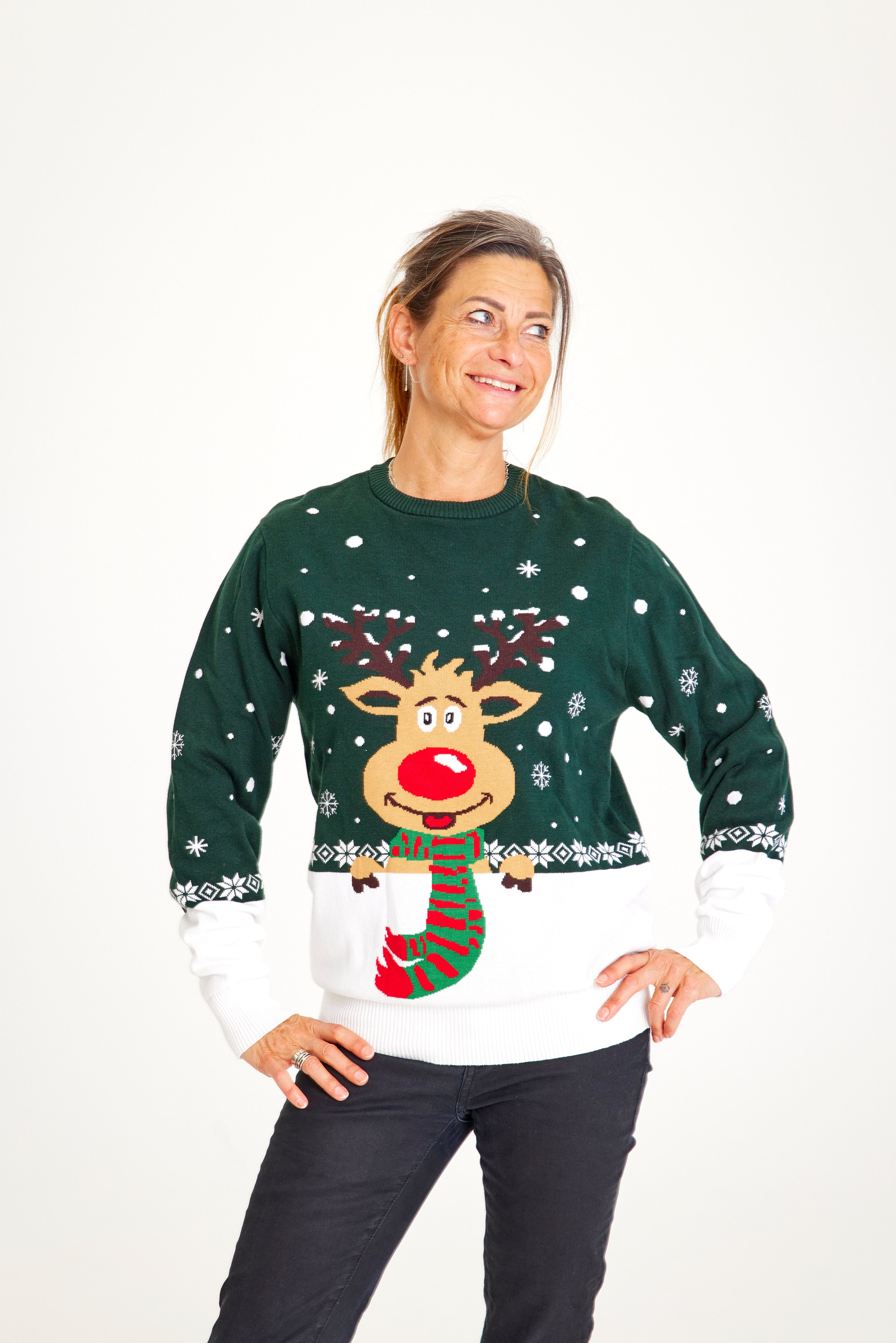 En smilende dame med hænderne i siden iført en grøn julesweater med Rudolf på.