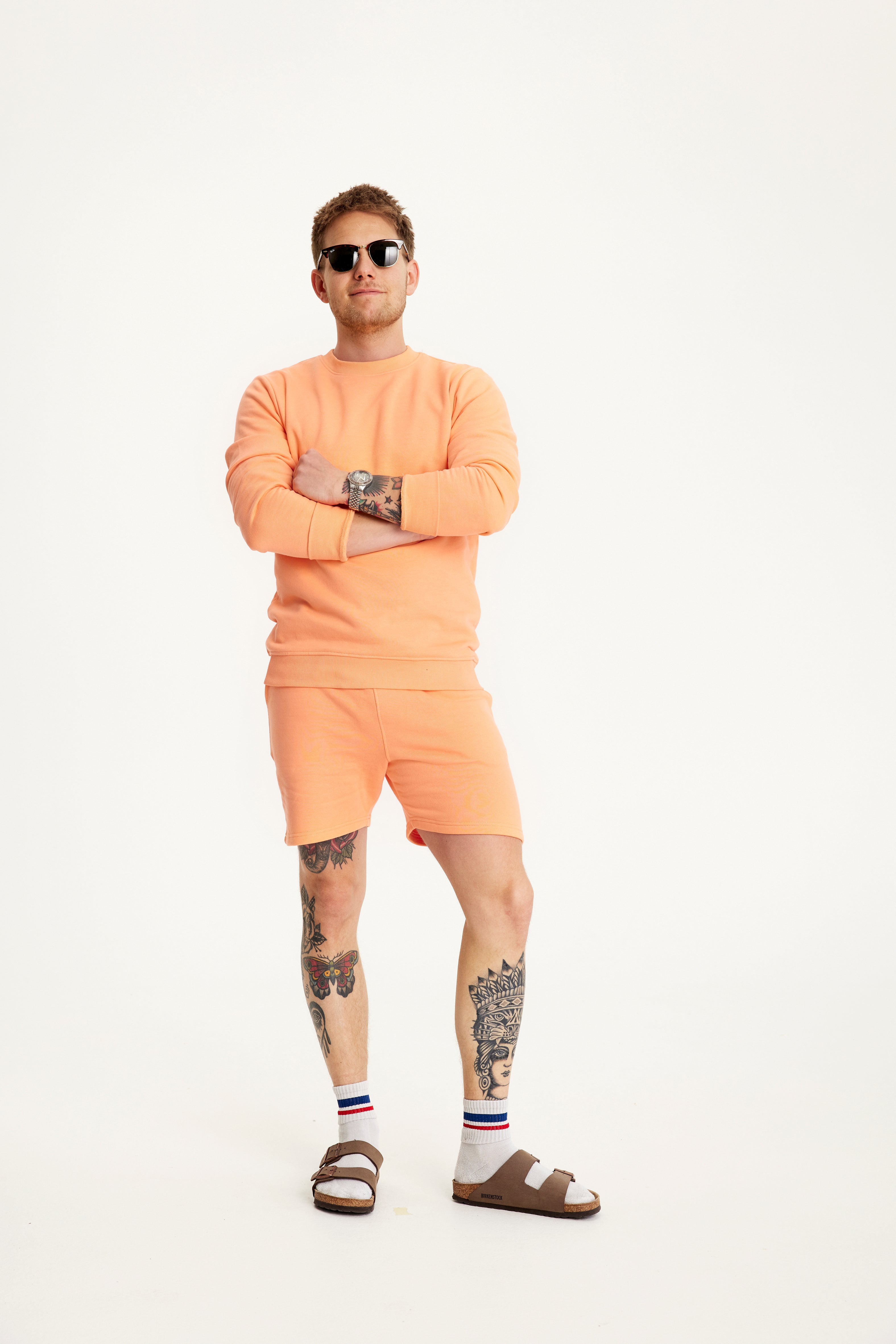 En mand med armene over kors er iført solbriller og et fint sommersæt.