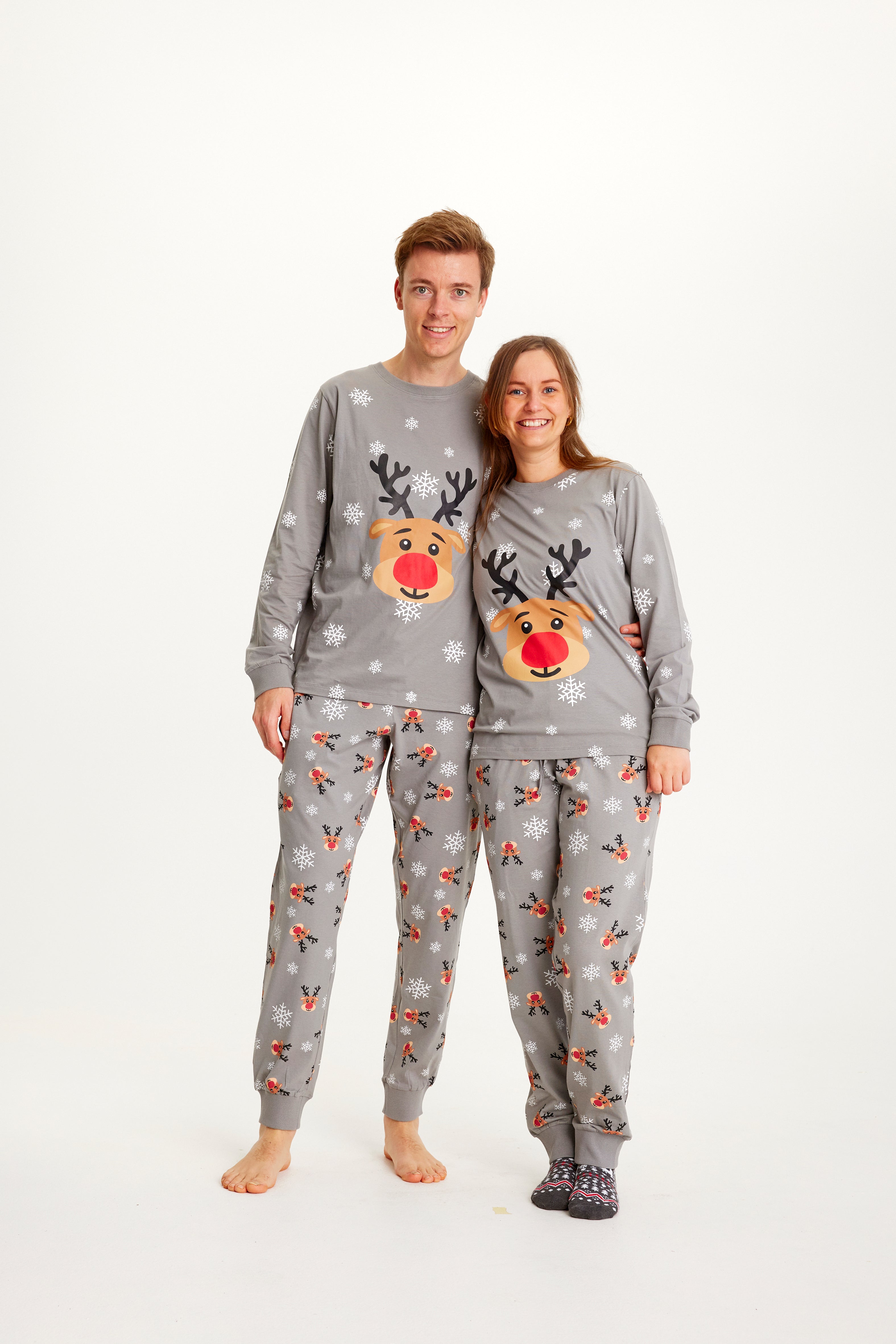 En mand og en dame iført grå julepyjamas med Rudolf på.