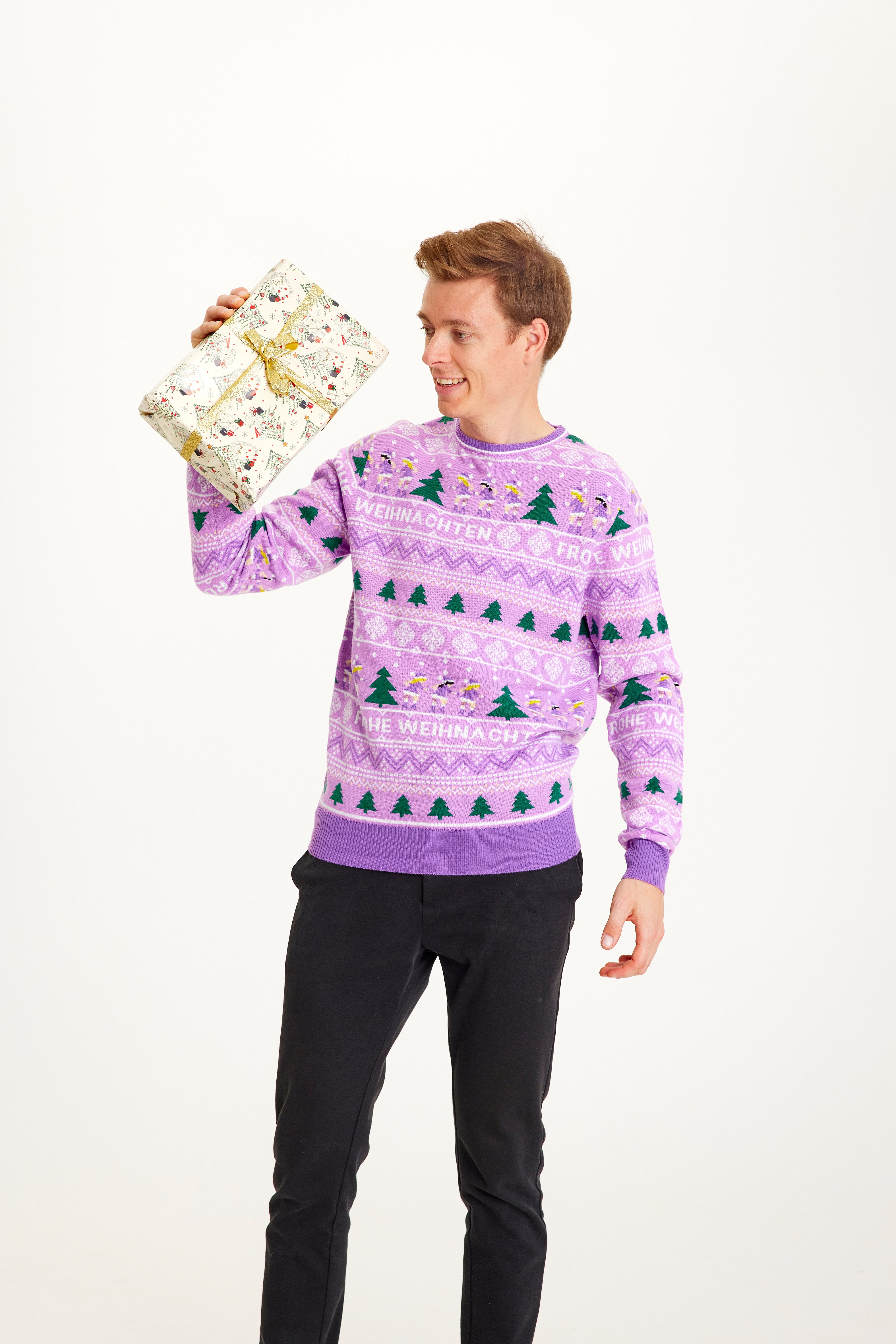 En mand iført en lilla julesweater og med en gave i den ene hånd.