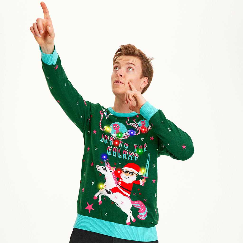 En mand i en grøn julesweater peger mod himlen.