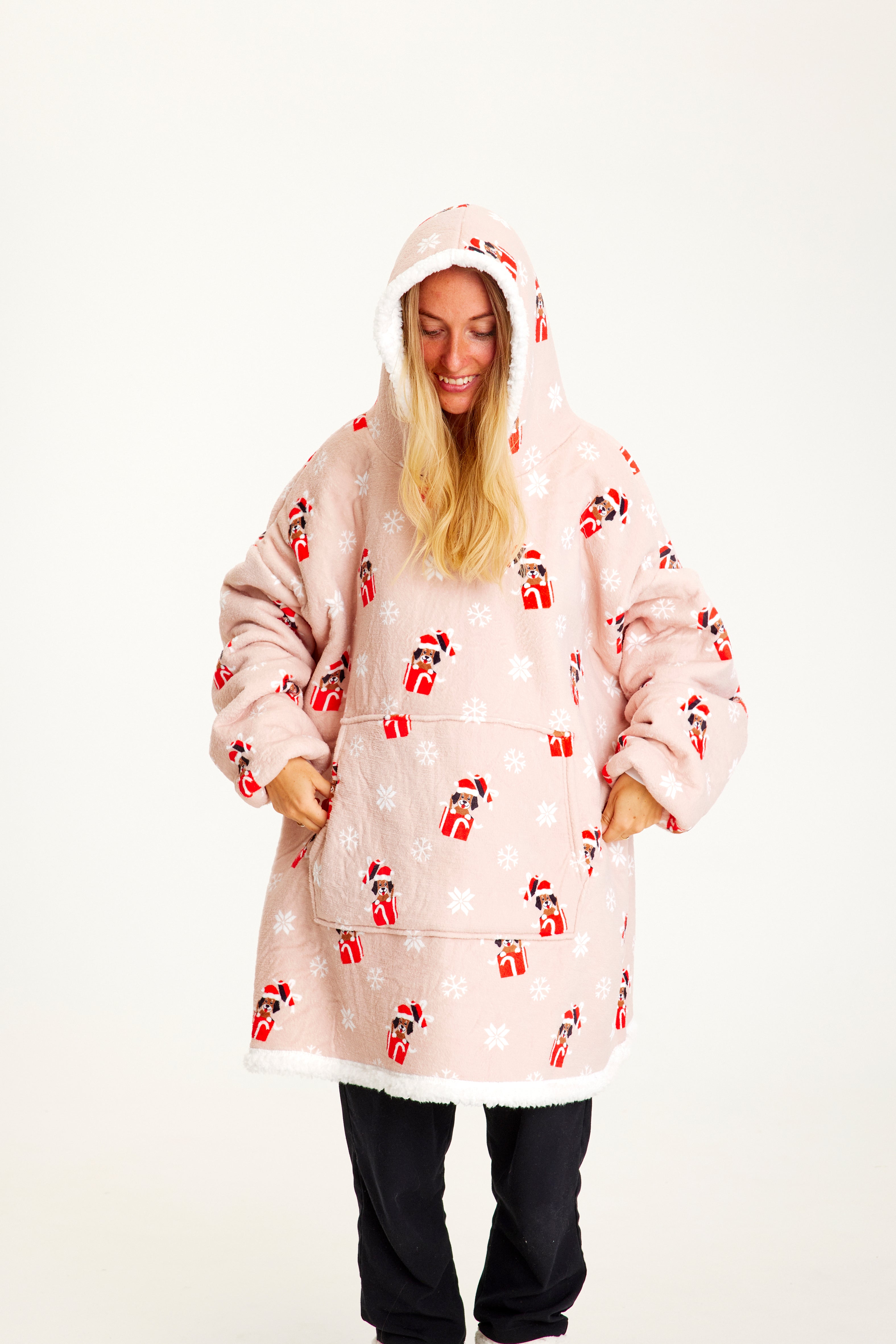 En smilende kvinde kigger nedad og er iført en lyserød julehoodie med  hunde.