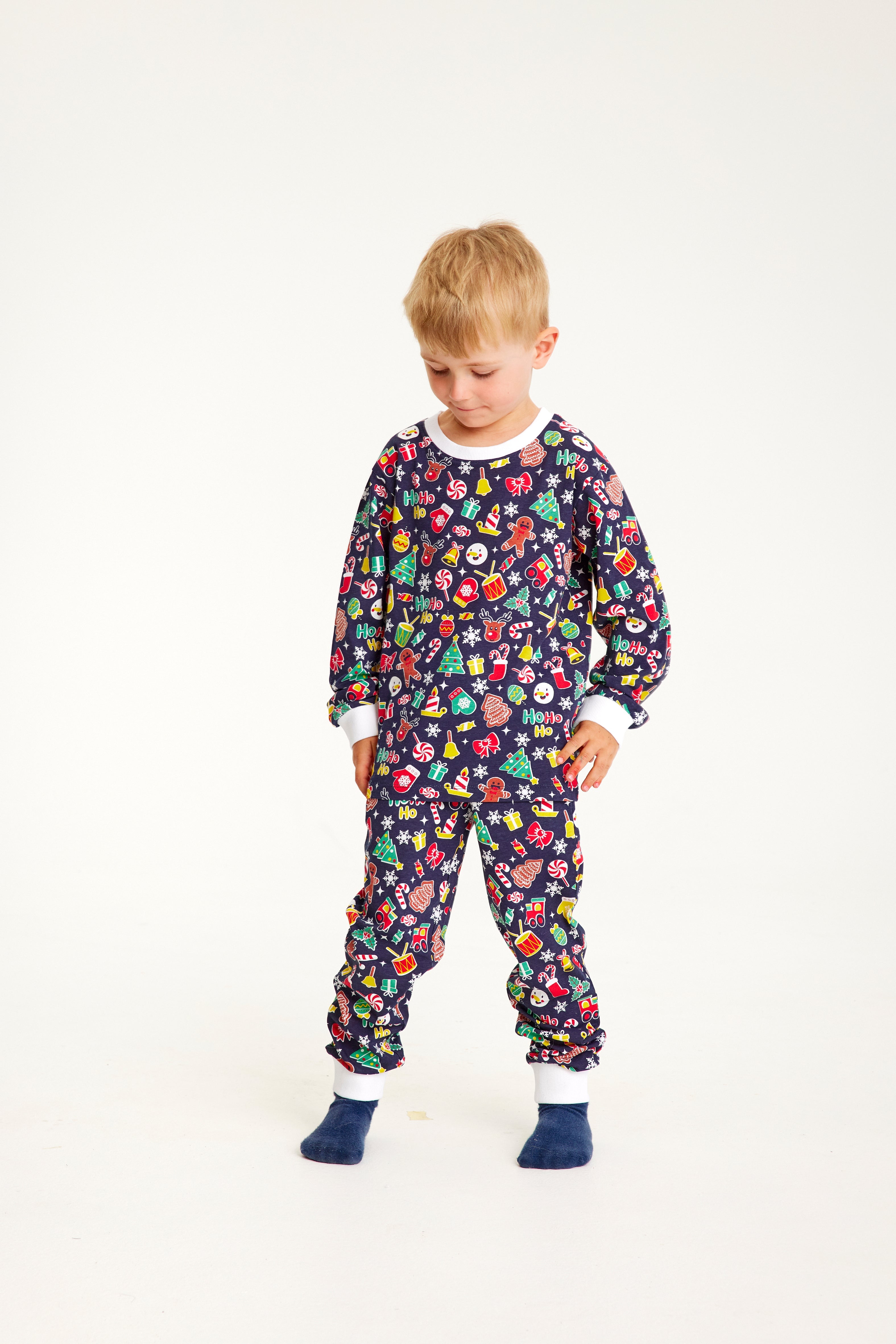 Et barn iført en blå julepyjamas med juletræer, klokker og vanter på.