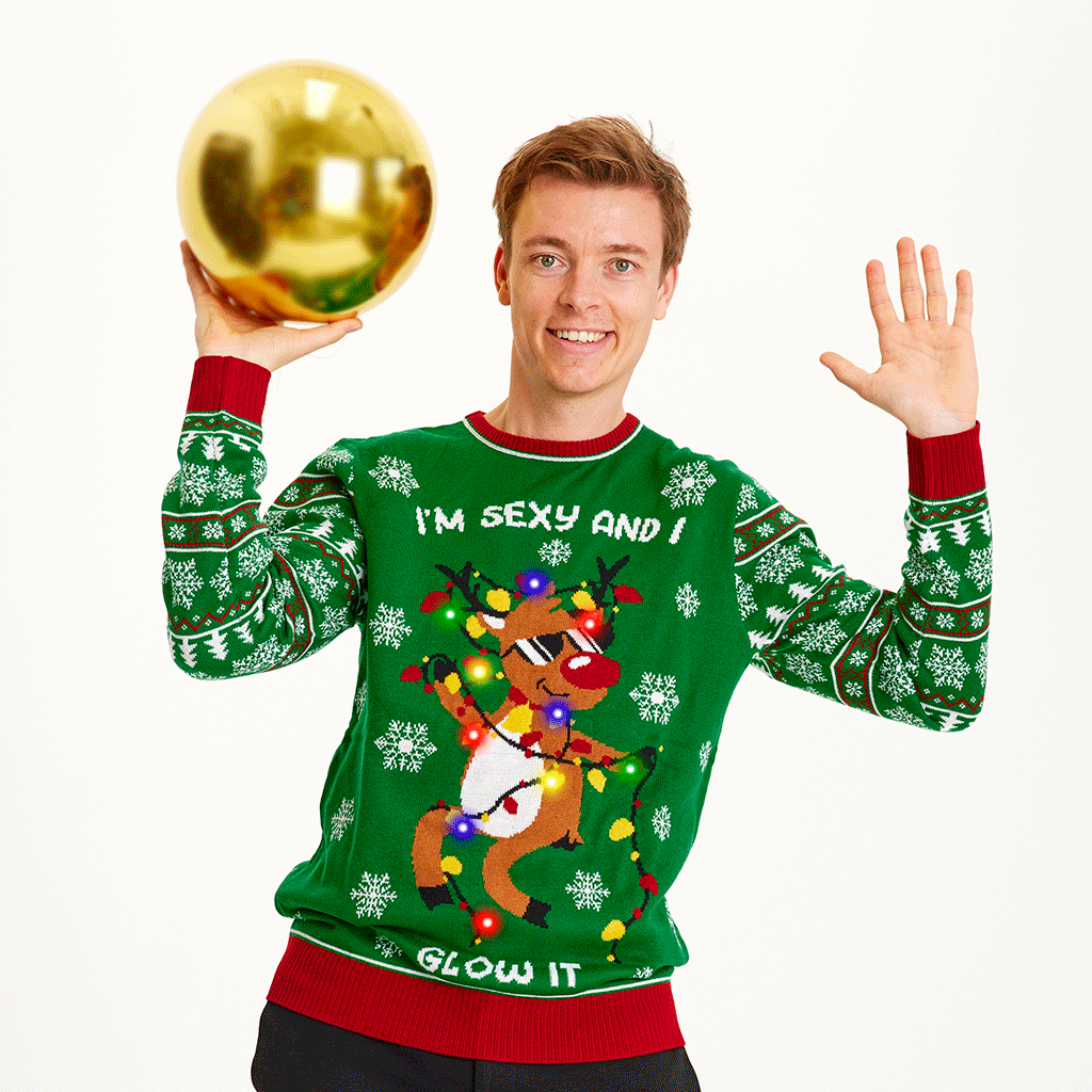 En mand med en stor, guldfarvet julekugle står i sin grønne julesweater med lys på.