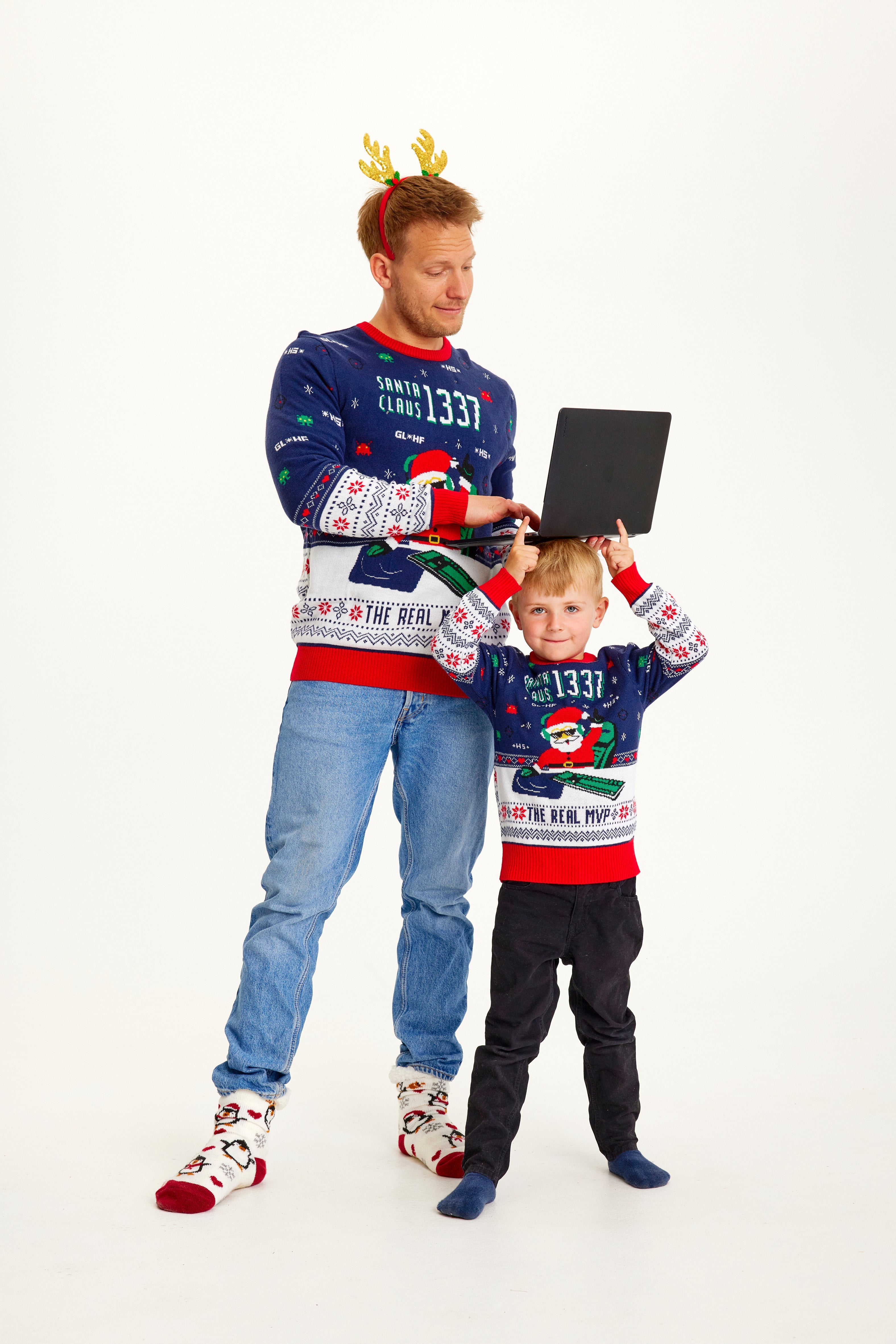 En mand med en computer og et barn iført matchende julesweatre.